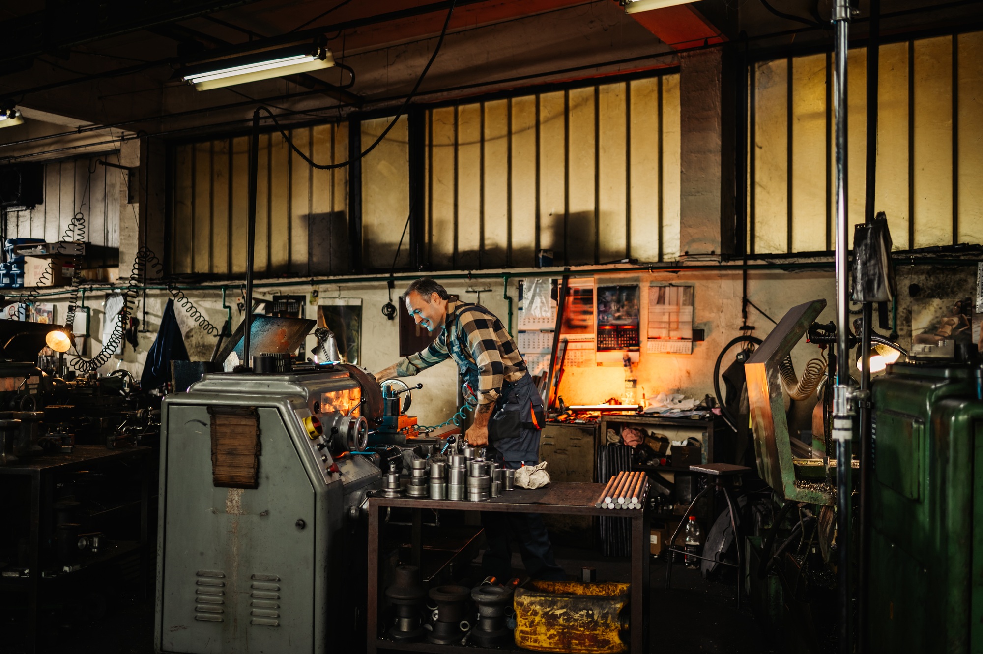Wide frame of a factory hangar with a machinist operating a lathe machine.